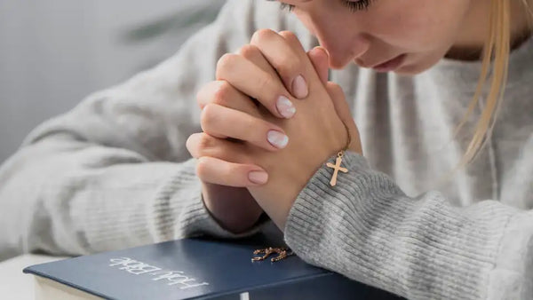 Woman holding on to a rose gold cross necklace to pray on a bible | Christian Jewelry | Glor-e