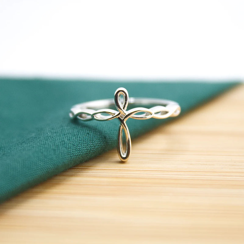 Silver cross-shaped Christian ring on a green fabric background | Glor-e