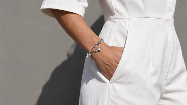 Woman wearing Glor-e's ENDLESS LOVE silver heart-link bracelet with a tailored white outfit.