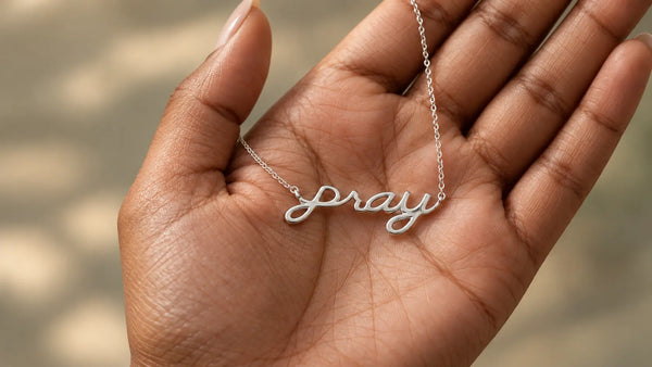 White gold PRAY Christian necklace resting naturally in a woman's open palm